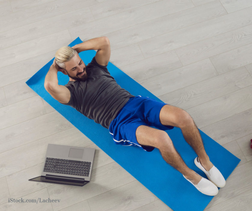 Mann liegt auf Matte und trainiert Bauchmuskeln daneben steht ein Laptop