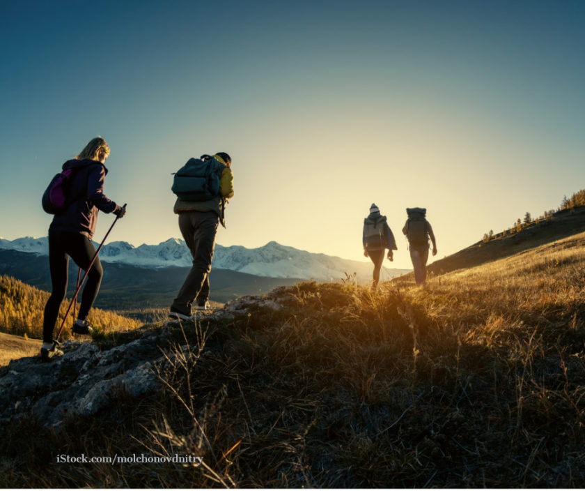 Vier Personen wandern einen Berg bei Sonnenaufgang hinauf.